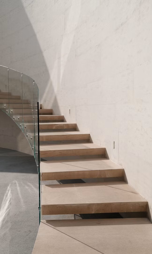 Curved staircase with glass railing, warm stone tones and soft daylight